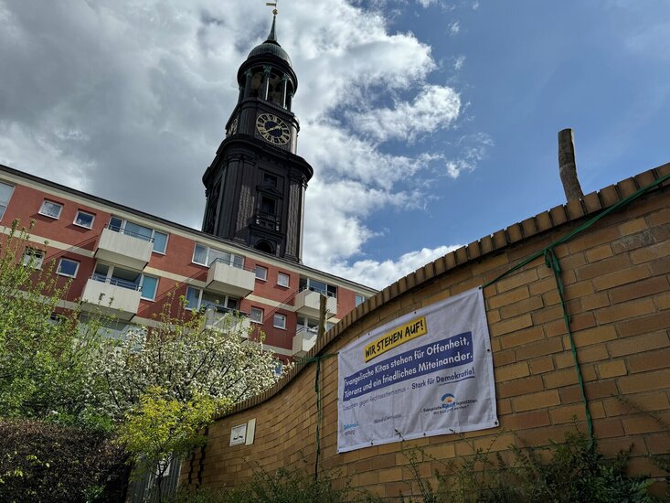 Ein Banner hängt an der Mauer einer Kita. Im Hintergrund ist der Turm der St. Michaelis Kirche in Hamburg zu sehen