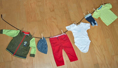 Eine Wäscheleine mit kleiner Kinderjacke, -mütze, -hose, -body, -socken und -shirt - Copyright: Daniela Steinke