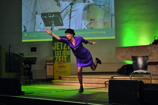 Eine in lila gekleidete Frau, in rennender Position auf einer Bühne mit grüner Beleuchtung - Copyright: Uwe Kirsch